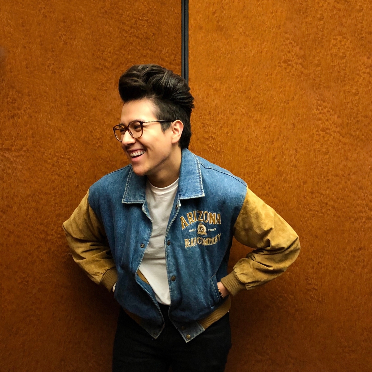 Antonio wears glasses and a denim jacket with suede sleeves, smiling away from the camera. 